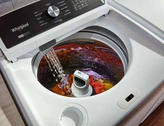 Whirlpool top-load washer filling with water, showing clothes circulating around the agitator.